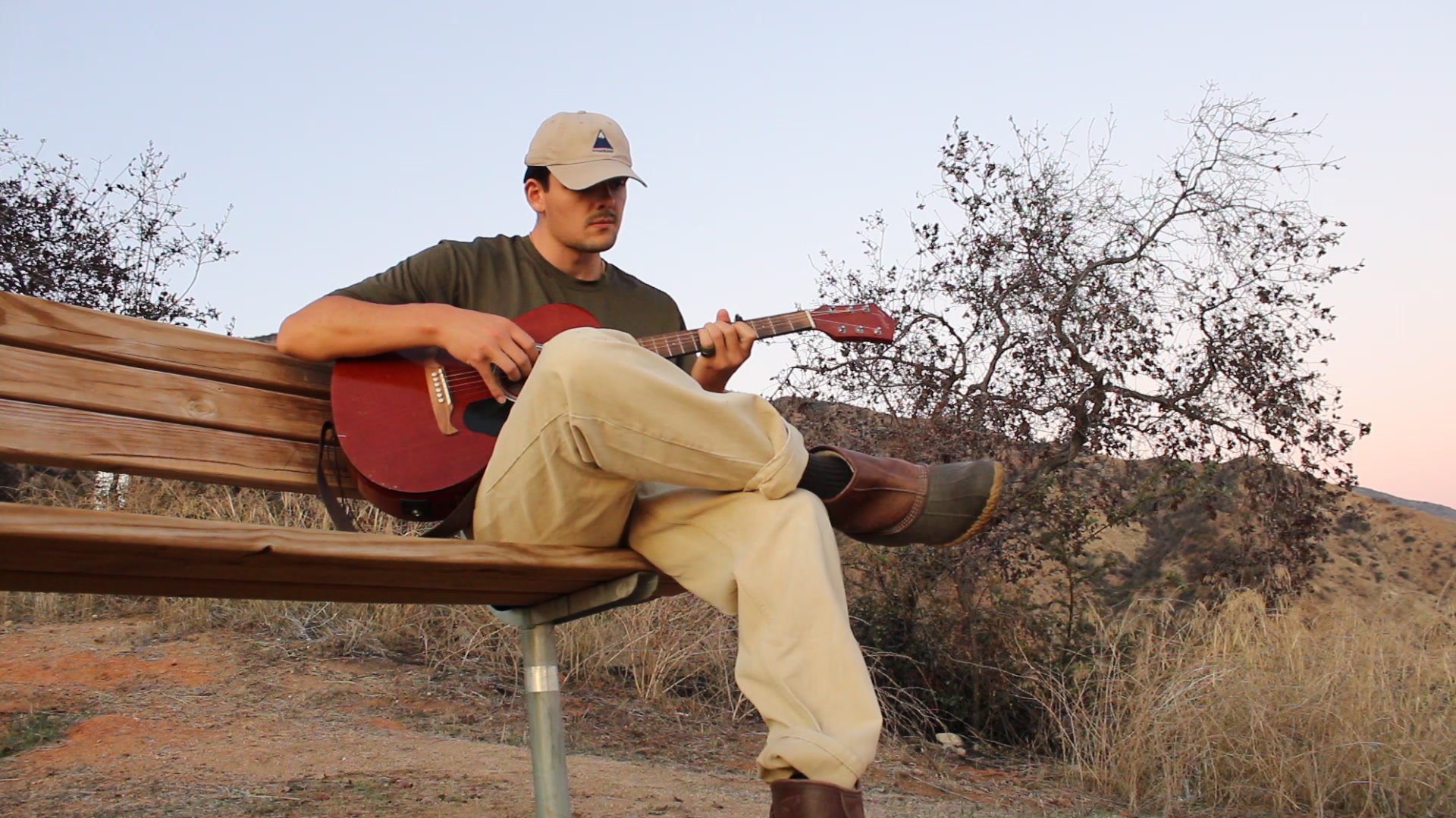 Alec From Maine sitting outdoors with a guitar